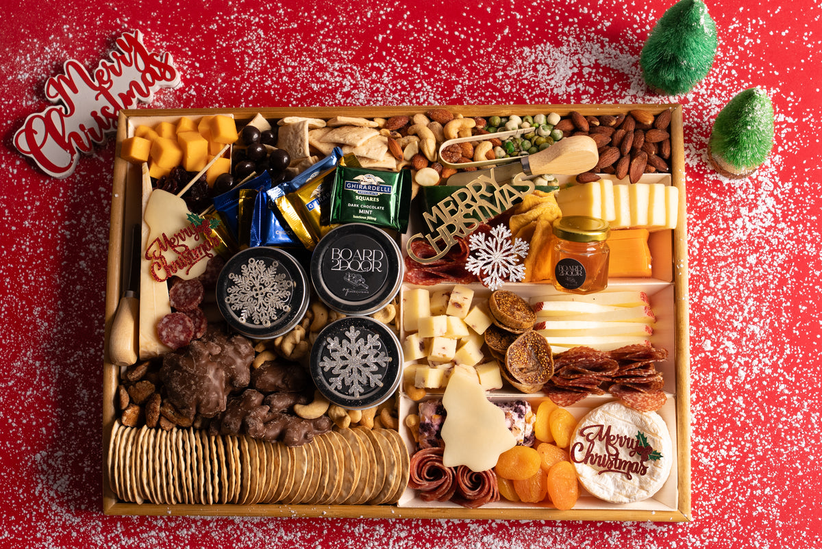 Gourmet food platter with various snacks and treats on a red background with Christmas decorations.