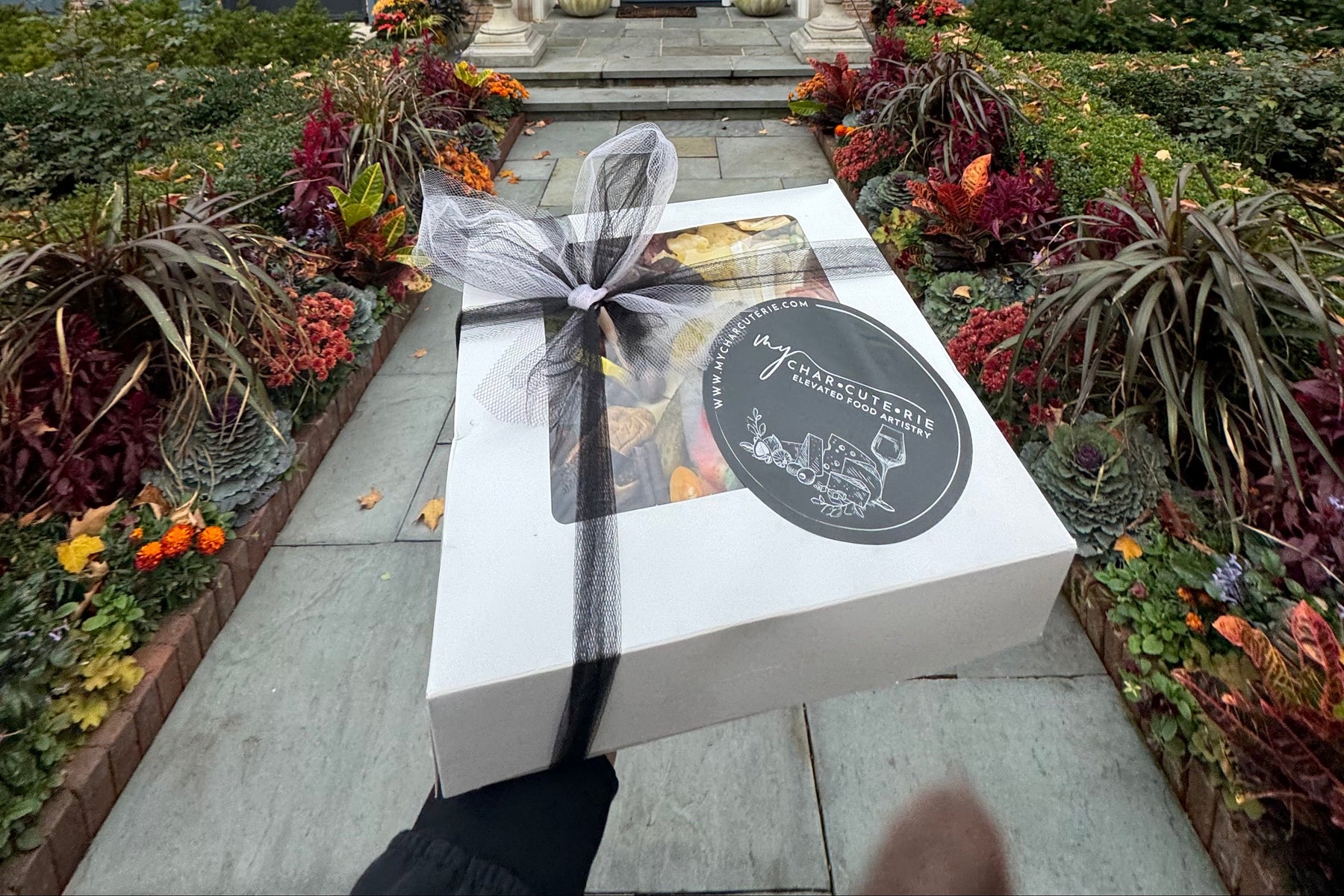 Gift box with a bow in front of a house with decorative plants